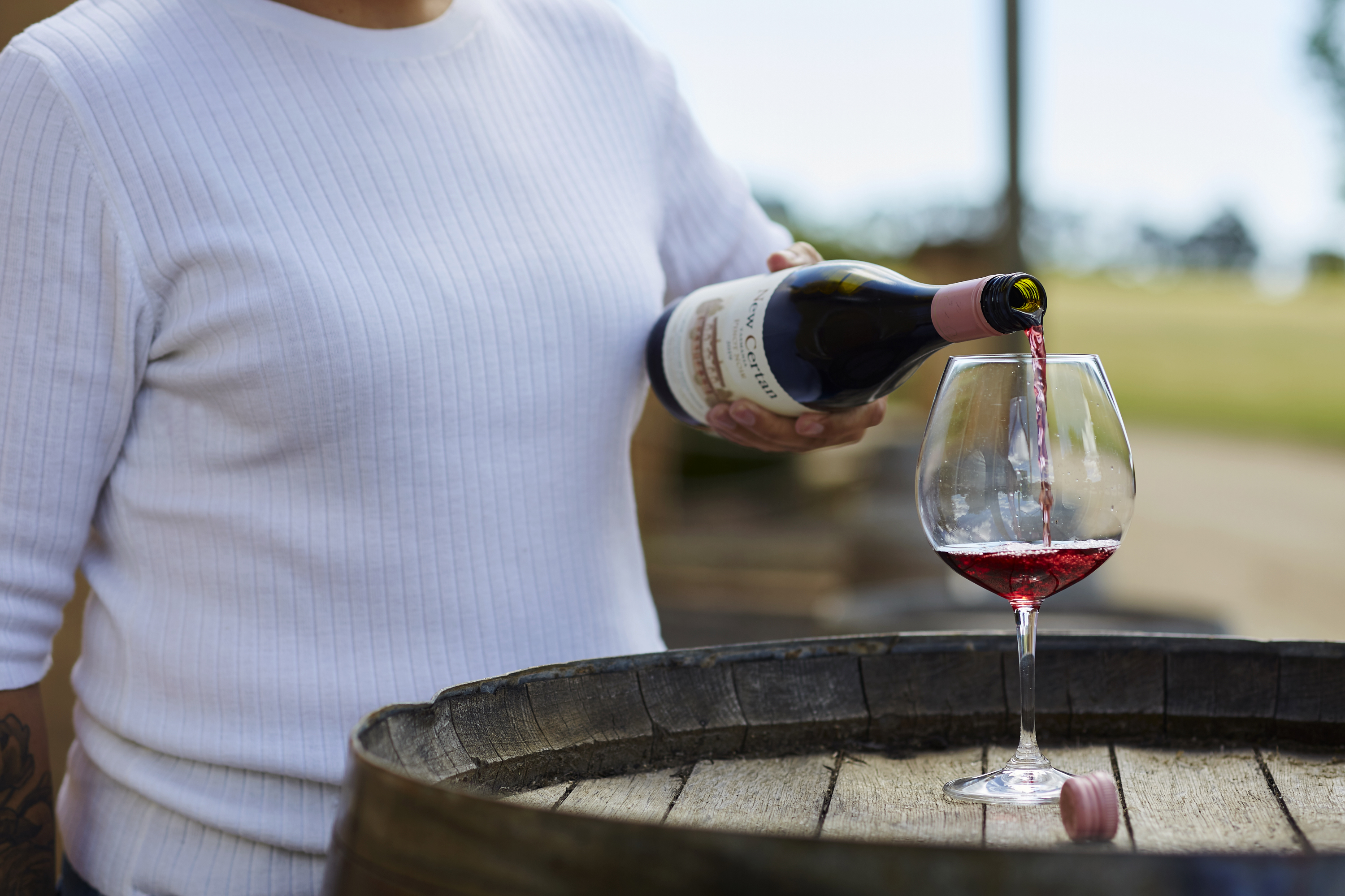Woman pouring wine into a wine glass on top of a barrel outdoors